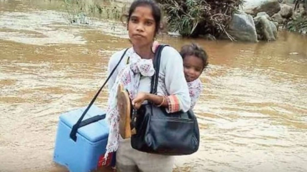 Viral Pic: हाथ में वैक्सीन कंटेनर, पीठ पर बच्चे को लेकर नदी पार करती स्वास्थ्यकर्मी की तस्वीर हुई वायरल